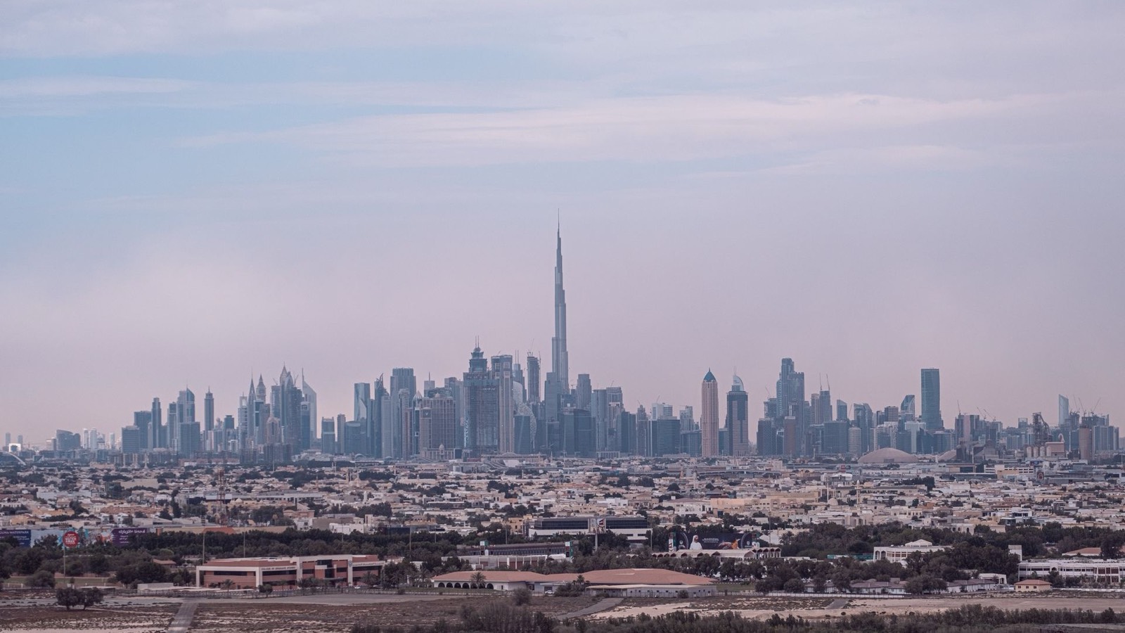 The Dubai skyline with the Burj Khalifa, seen across low-rise neighbourhoods under a cloudy sky
