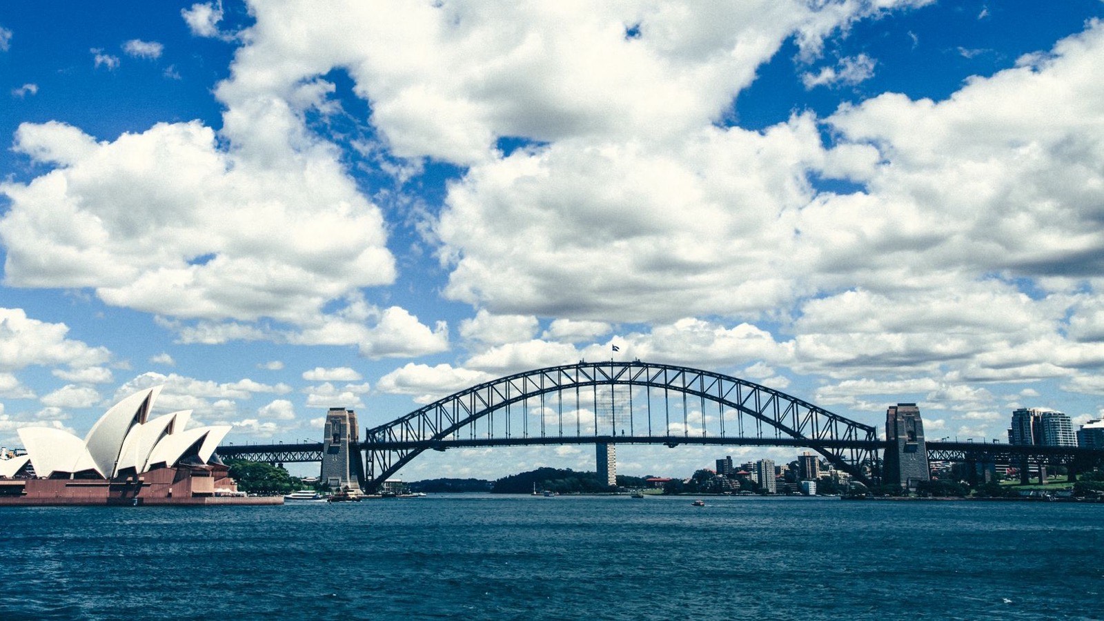 Sydney Opera House and Sydney Harbour Bridge across the harbour under a blue sky with white clouds