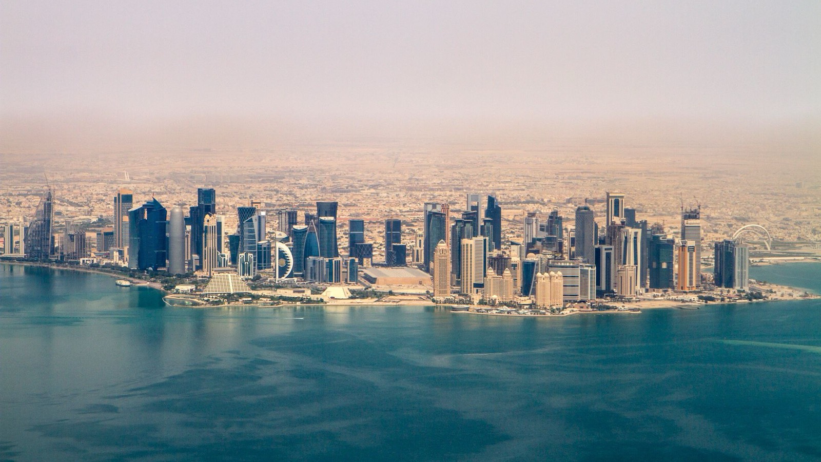 Aerial view of the Doha skyline in Qatar, with towers along the bay under a hazy sky